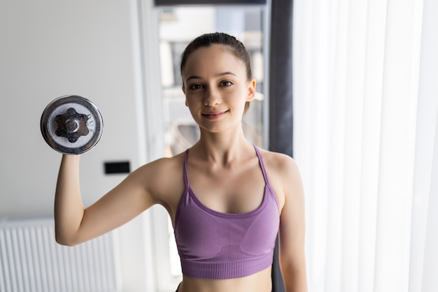 Mujer joven está haciendo ejercicio con pesas en casa.