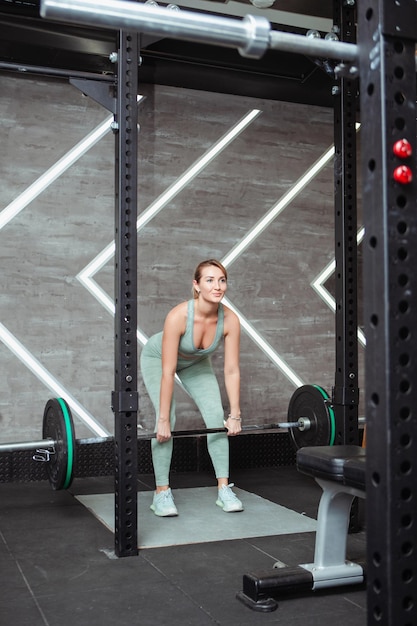 Una mujer joven está haciendo ejercicios de fitness con barra en el gimnasio