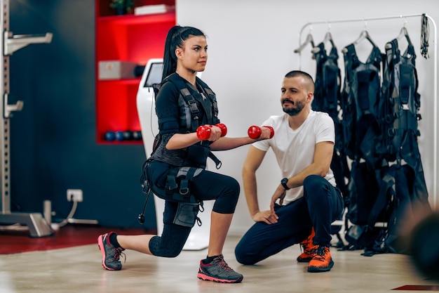 Mujer joven está haciendo entrenamiento personal EMS con entrenador en el gimnasio.