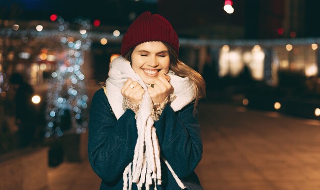 La mujer joven está llena de felicidad, caminando al aire libre en la calle, vistiendo ropa de invierno en Navidad