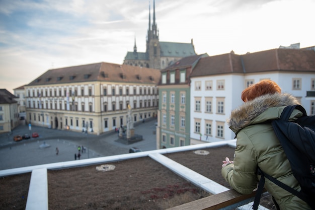 La mujer joven está mirando a Brno desde una terraza de observación. Tome fotos de la ciudad por teléfono y compártalas en el sitio social