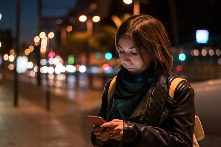 La mujer joven está mirando su teléfono inteligente en la noche.