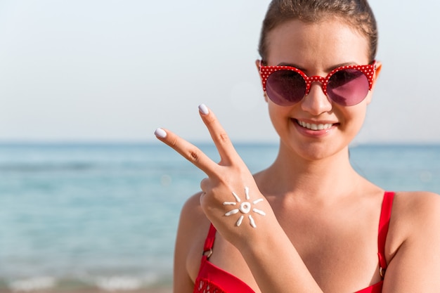 La mujer joven está mostrando un gesto de paz y tiene forma de sol en su mano en la playa.