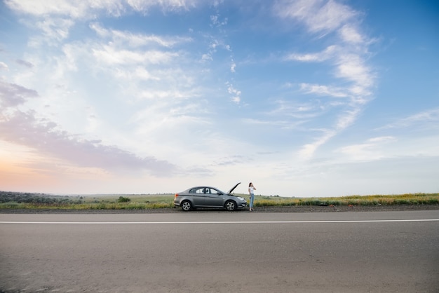 Una mujer joven está parada cerca de un automóvil averiado.