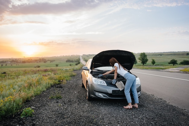 Una mujer joven está parada cerca de un automóvil averiado.