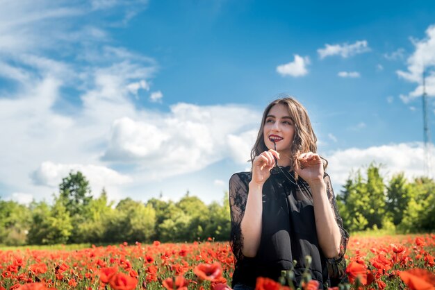 Mujer joven está de pie cerca del campo floreciente de amapolas