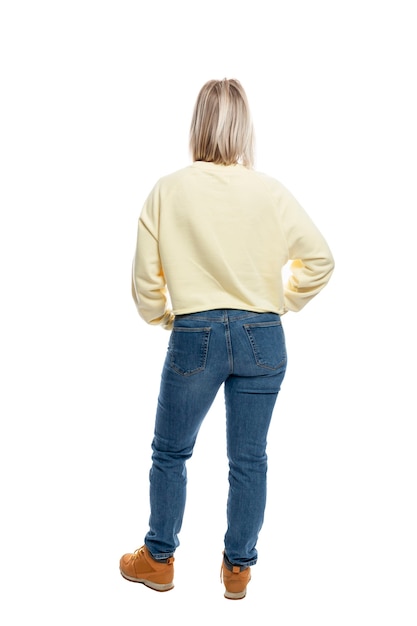 Una mujer joven está de pie con la espalda en pleno crecimiento. Rubia sonriente con un suéter amarillo y jeans.