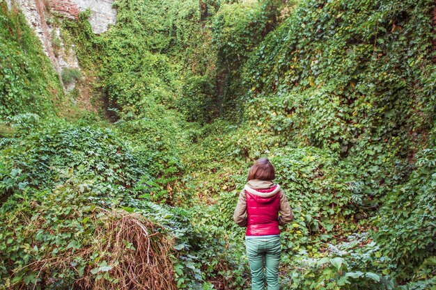 Una mujer joven está de pie frente a las hojas crecidas y verdes. Humanos y la naturaleza.