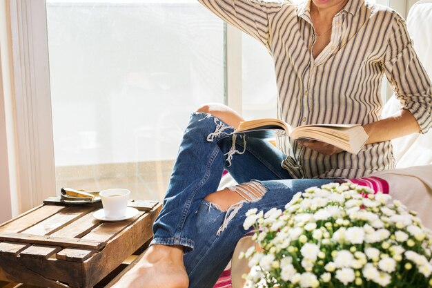 Mujer joven se está relajando en casa bebiendo té libro de lectura