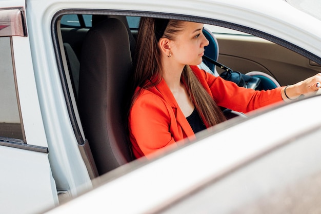 Una mujer joven está sentada al volante de un automóvil. Gestión del transporte. El tema de viajar en automóvil.
