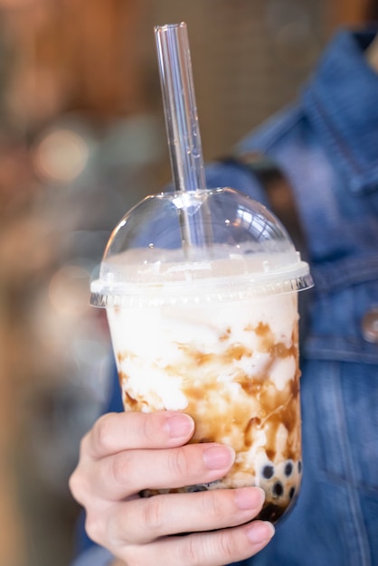 Mujer joven está sosteniendo beber té de leche de burbuja de perlas de tapioca con sabor a azúcar moreno con paja de vidrio en el mercado nocturno de Taiwán cerca de bokeh