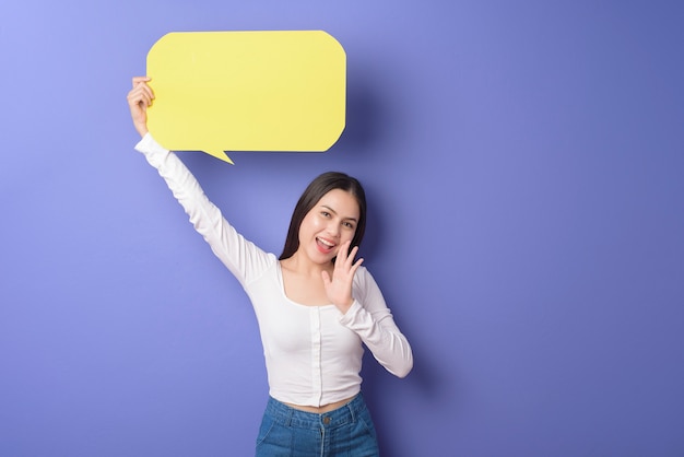 La mujer joven está sosteniendo discurso vacío amarillo sobre fondo púrpura