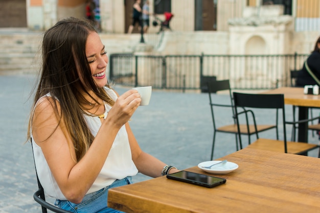 La mujer joven está sosteniendo una taza de café mientras ella está sonriendo.