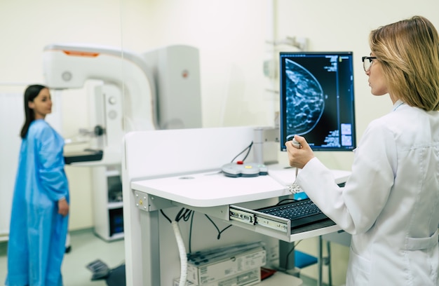 La mujer joven está teniendo un examen de mamografía en el hospital o en una clínica privada con una doctora profesional.