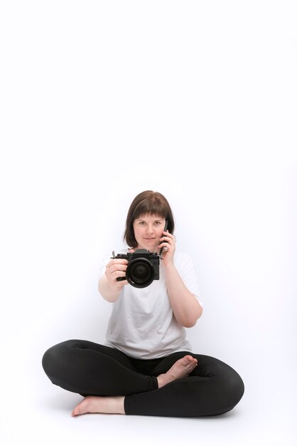 Mujer joven está tomando fotografías al mismo tiempo en la cámara y hablando por teléfono, posición de loto. Equilibrio laboral