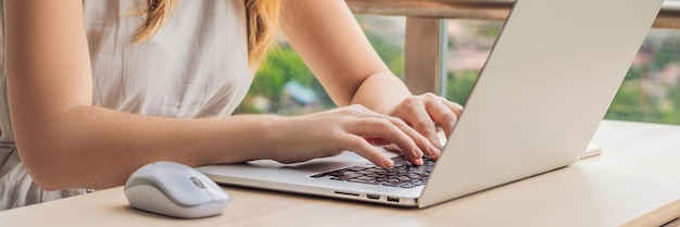 Mujer joven está trabajando en una computadora portátil en su balcón con vista a los rascacielos trabajo remoto independiente