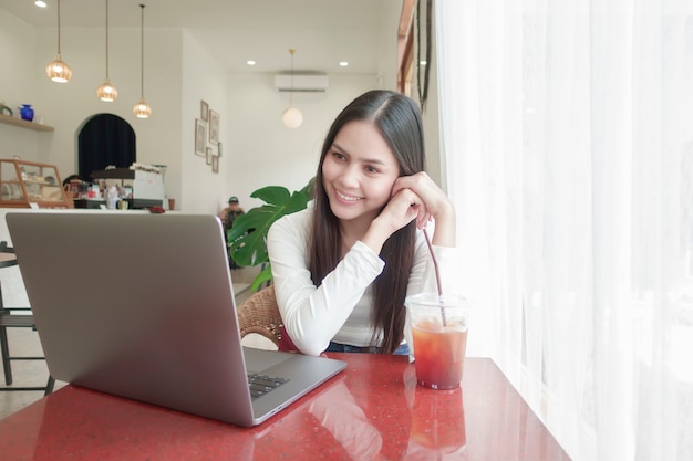 Una mujer joven está trabajando con su computadora portátil en la cafetería.