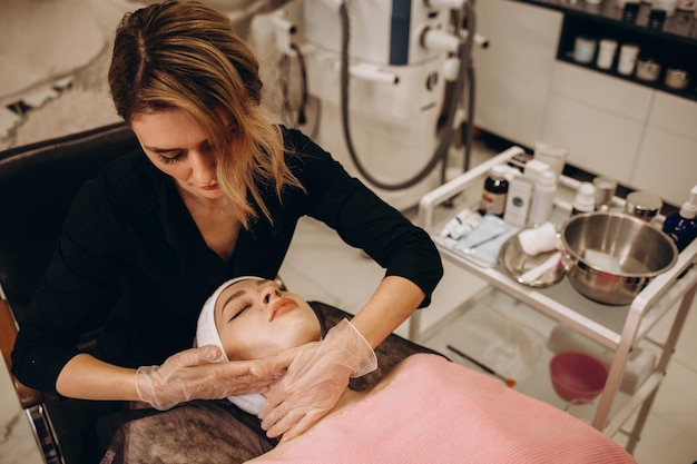 Mujer joven esteticista está haciendo el procedimiento de limpieza en el salón de belleza Cuidado de la piel facial Procedimiento de limpieza Cosmetología