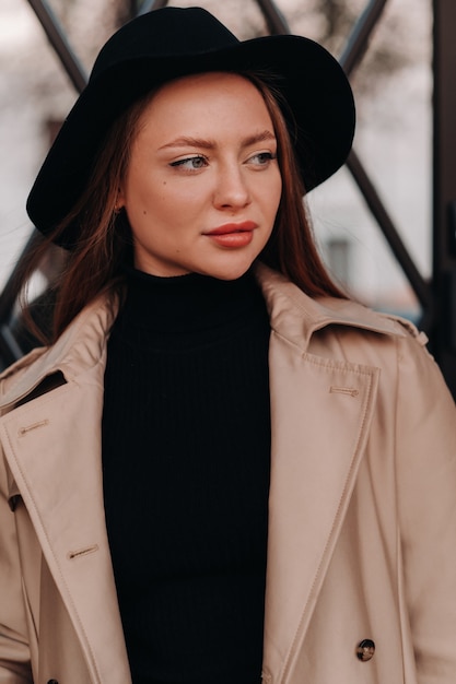 Mujer joven con estilo en un abrigo beige con un sombrero negro en una calle de la ciudad. Moda de calle femenina. Ropa de otoño Estilo urbano.