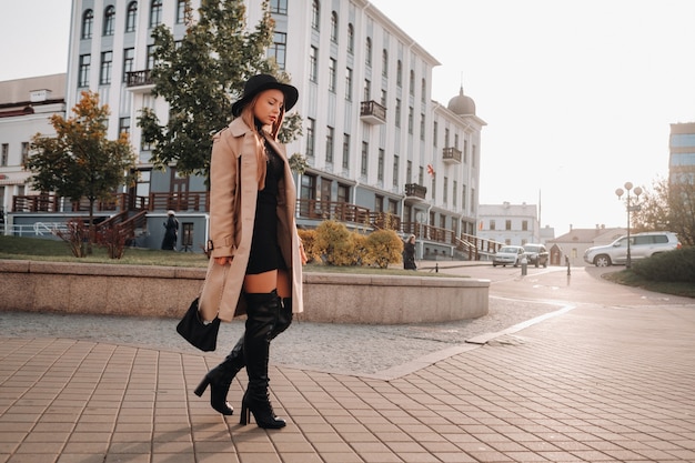 Mujer joven con estilo con un abrigo beige con un sombrero negro en una calle de la ciudad. Moda urbana femenina. Ropa de otoño Estilo urbano.