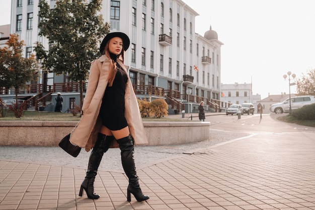 Mujer joven con estilo con un abrigo beige con un sombrero negro en una calle de la ciudad. Moda urbana femenina. Ropa de otoño Estilo urbano.