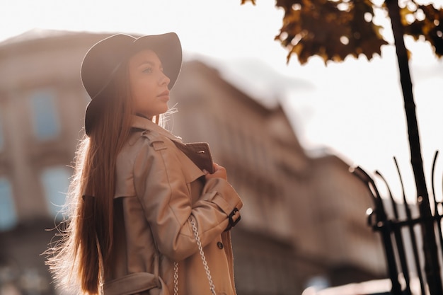 Mujer joven con estilo con un abrigo beige con un sombrero negro en una calle de la ciudad. Moda urbana femenina. Ropa de otoño Estilo urbano.