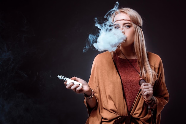 Mujer joven en el estilo boho que sopla humo