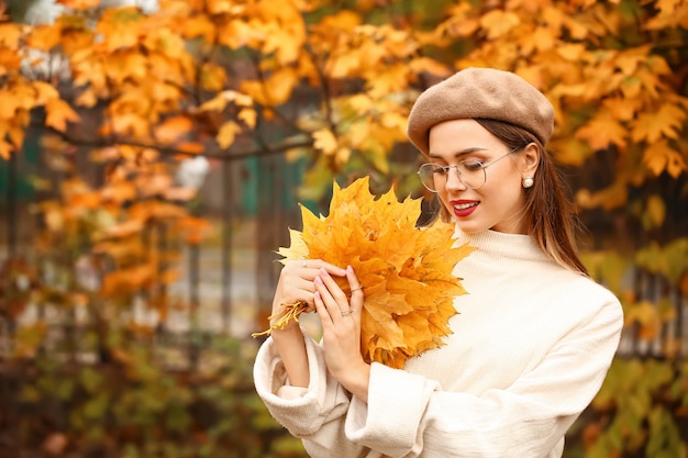 Mujer joven con estilo con hojas en el parque otoño