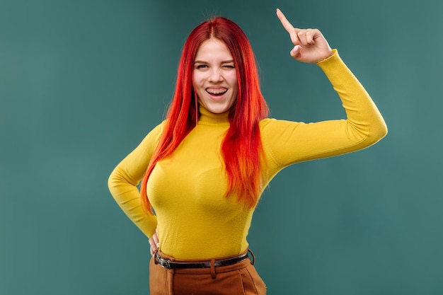 Mujer joven con estilo con el pelo largo y rojo con suéter amarillo posando emocionalmente en el fondo del estudio