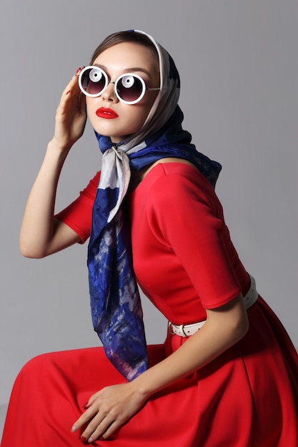 Mujer joven en estilo retro con gafas de sol y pañuelo de seda. Mujer retro de moda estilo años sesenta.