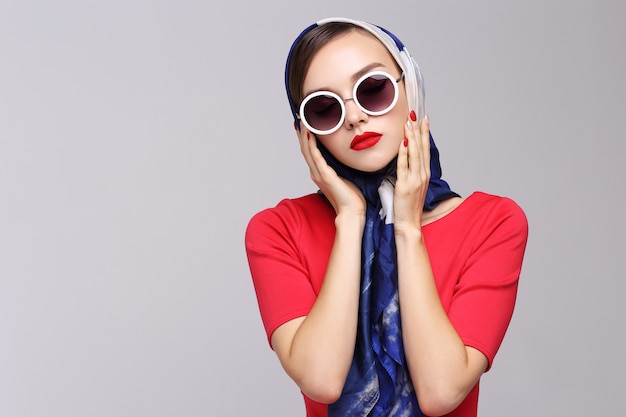 Mujer joven en estilo retro con gafas de sol y pañuelo de seda. Mujer retro de moda estilo años sesenta.