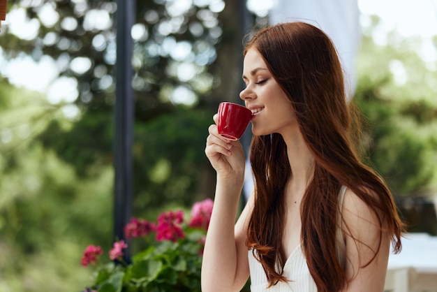 Mujer joven con estilo en un vestido blanco bebe café al aire libre en un café mujer feliz relajante