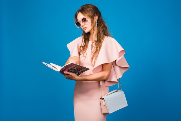 Mujer joven con estilo en vestido rosa de lujo leyendo un libro