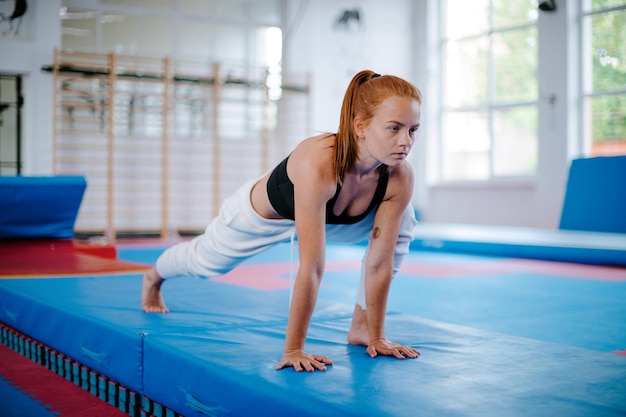 Mujer joven se estira en una alfombra y mira hacia adelante en el gimnasio antes del ejercicio foto de alta calidad
