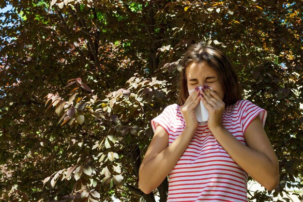 Foto mujer joven estornudando mientras está de pie contra las plantas en el parque