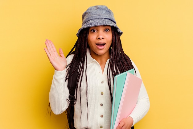 Mujer joven estudiante afroamericana aislada en la pared amarilla sorprendida y conmocionada