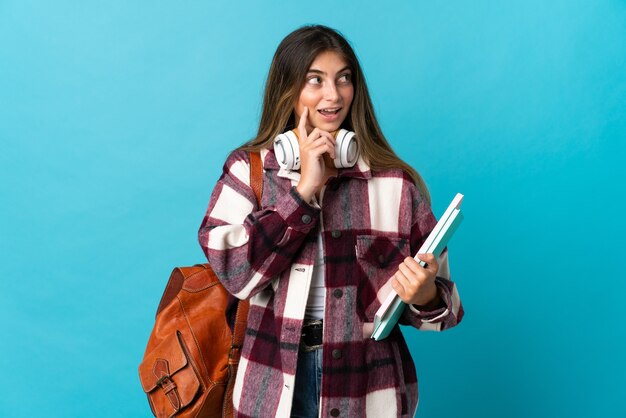 Mujer joven estudiante aislada en azul pensando en una idea mientras mira hacia arriba