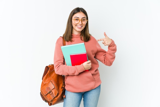 Mujer joven estudiante aislada en blanco bakcground persona apuntando con la mano a un espacio de copia de camisa, orgulloso y seguro