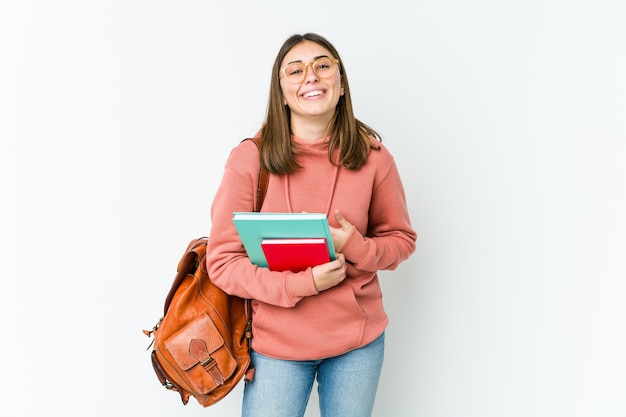 Mujer joven estudiante aislada en blanco bakcground se ríe felizmente y se divierte manteniendo las manos en el estómago