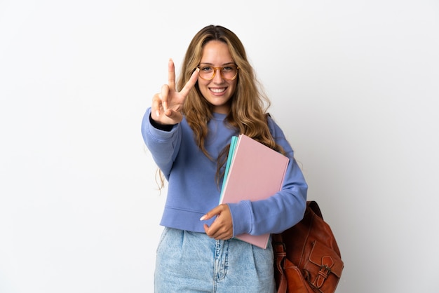 Mujer joven estudiante aislada en blanco sonriendo y mostrando el signo de la victoria