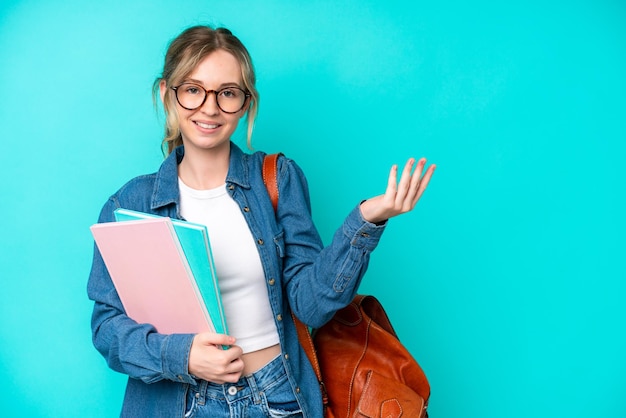 Mujer joven estudiante aislada de fondo azul extendiendo las manos a un lado para invitar a venir