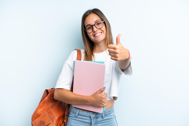 Mujer joven estudiante aislada de fondo azul con los pulgares hacia arriba porque algo bueno ha sucedido