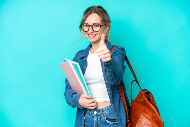 Mujer joven estudiante aislada de fondo azul con los pulgares hacia arriba porque algo bueno ha sucedido