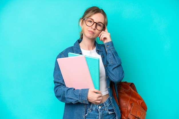 Mujer joven estudiante aislada de fondo azul que tiene dudas y piensa