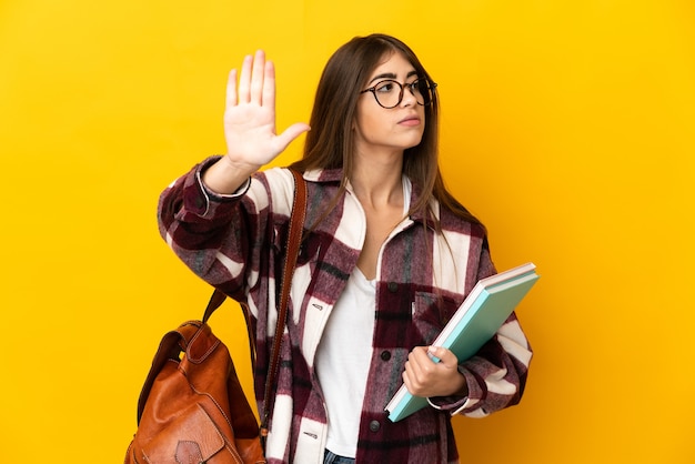 Foto mujer joven estudiante aislada en la pared amarilla haciendo gesto de parada y decepcionado