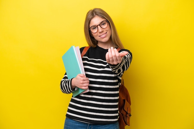 Mujer joven estudiante aislada sobre fondo amarillo invitando a venir con la mano Feliz de que hayas venido