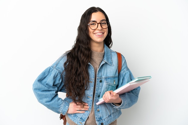 Mujer joven estudiante aislada sobre fondo blanco posando con los brazos en la cadera y sonriendo