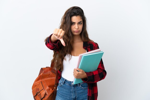 Mujer joven estudiante aislada sobre fondo blanco que muestra el pulgar hacia abajo con expresión negativa