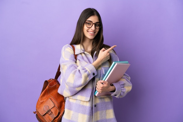 Mujer joven estudiante aislada sobre fondo púrpura apuntando hacia el lado para presentar un producto