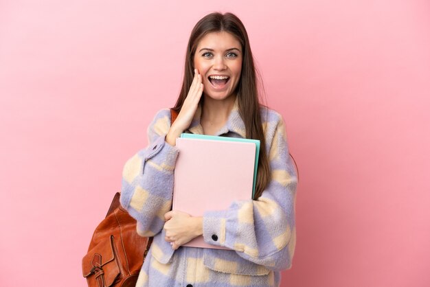 Mujer joven estudiante aislada sobre fondo rosa con sorpresa y expresión facial conmocionada